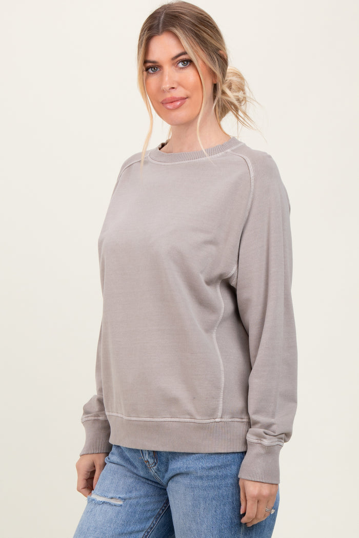 woman wearing a taupe oversized sweatshirt with a scoop neckline and long sleeves paired with distressed blue jeans