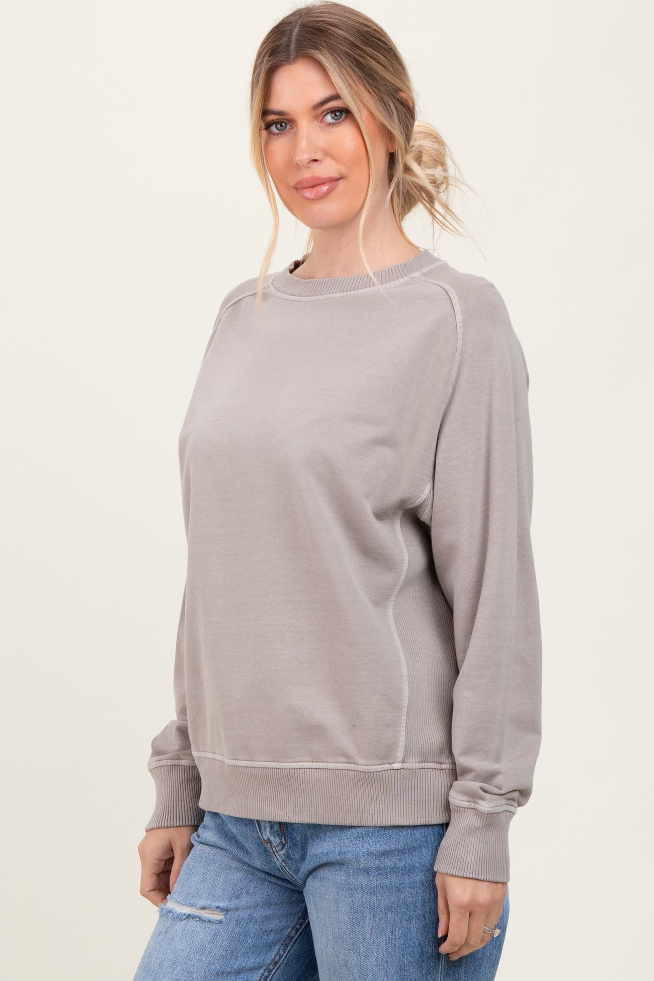 woman wearing a taupe oversized sweatshirt with a scoop neckline and long sleeves paired with distressed blue jeans