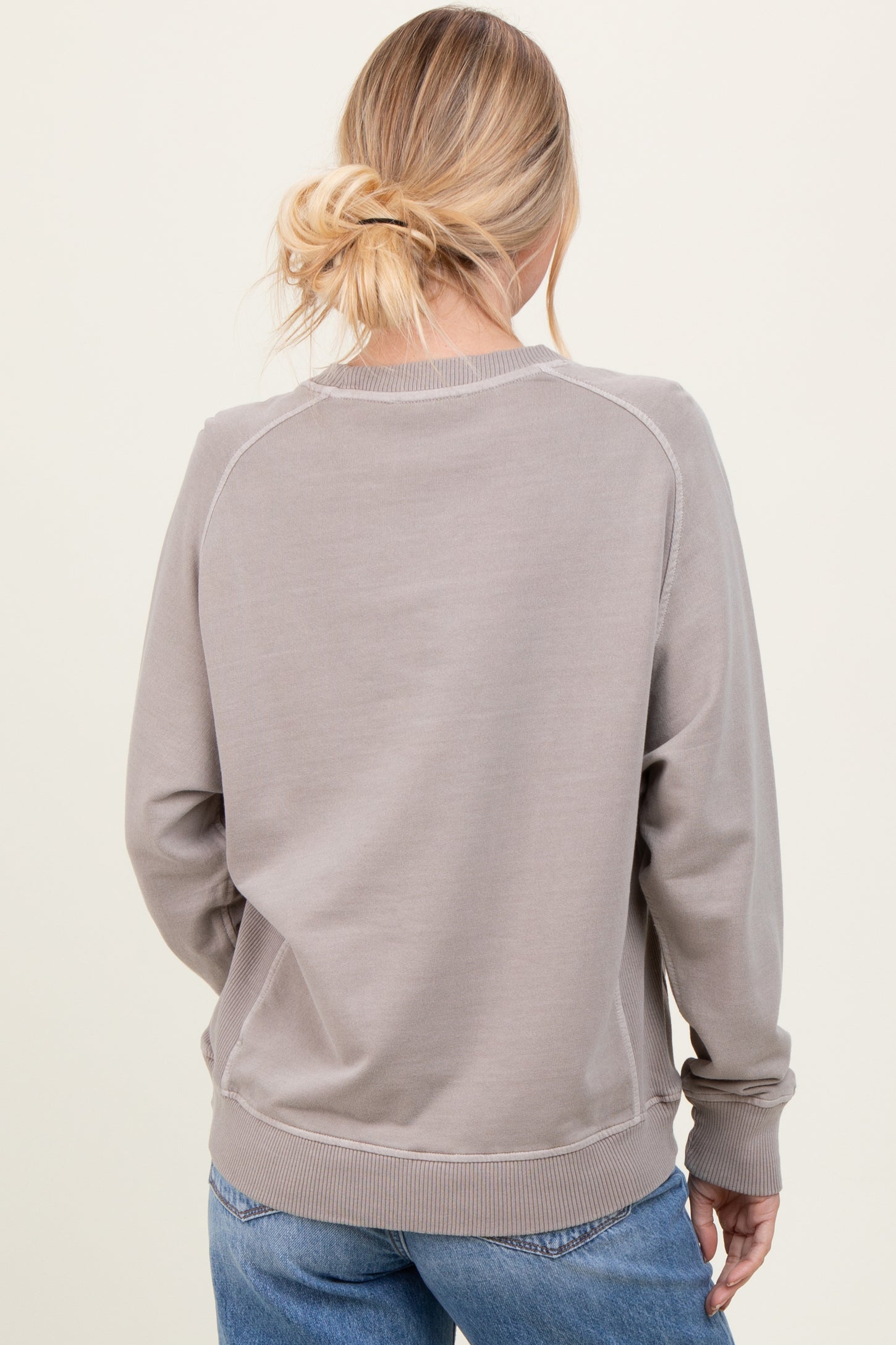 woman wearing a taupe cozy sweatshirt with a relaxed fit and ribbed cuffs, seen from the back