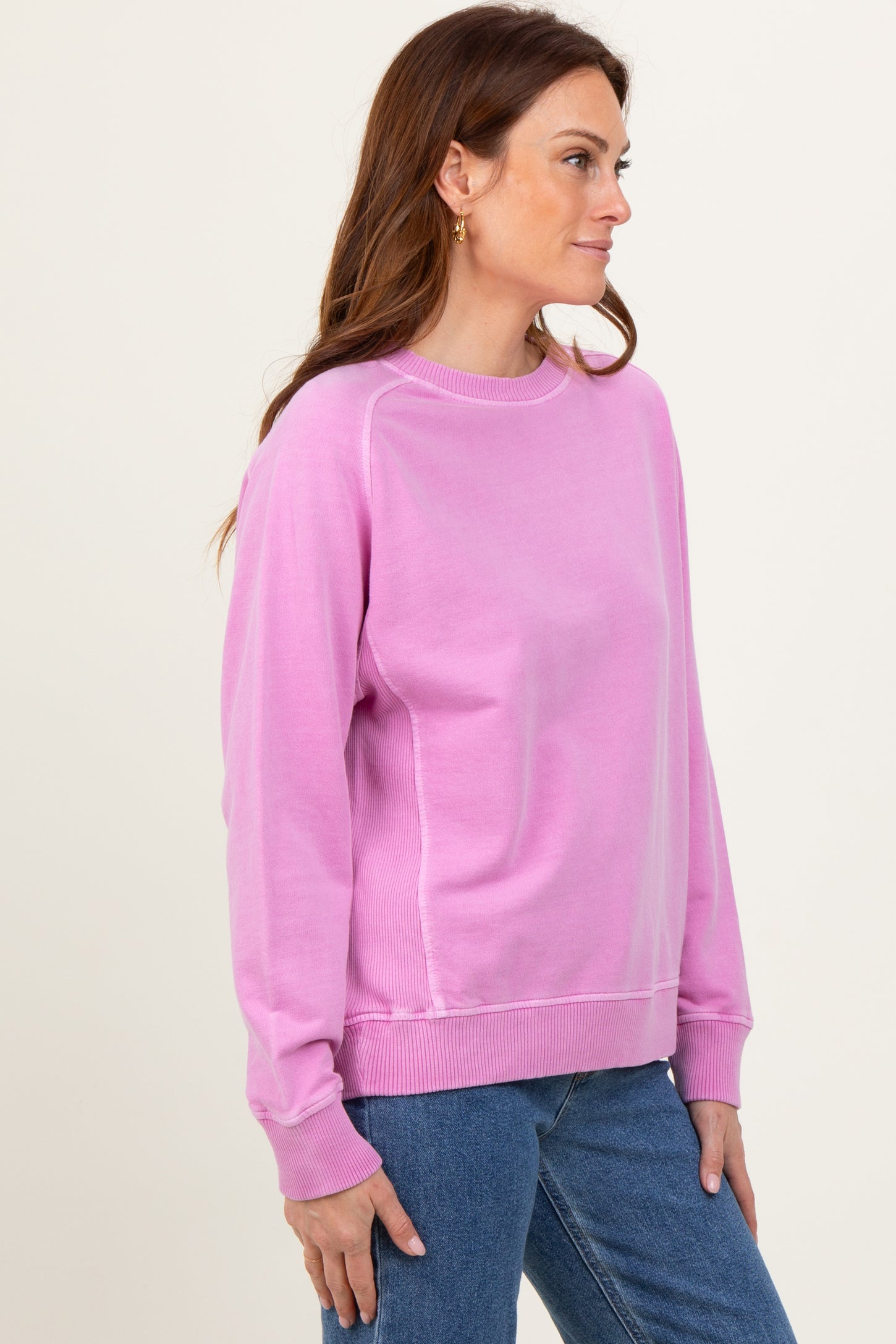 woman wearing a pink long sleeve sweatshirt with ribbed details and relaxed fit paired with blue jeans
