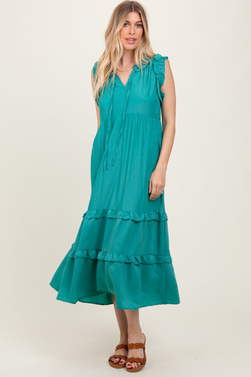 woman wearing a turquoise midi dress with ruffle details and a tie neck, standing against a neutral background