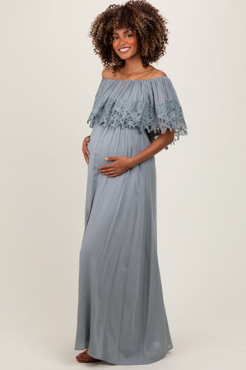 woman wearing a light gray off-the-shoulder maternity gown with lace details and holding her baby bump