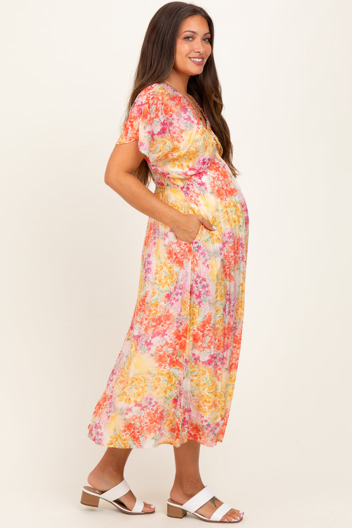 woman wearing a floral print maternity dress in yellow and pink with short sleeves and pockets, highlighting her baby bump