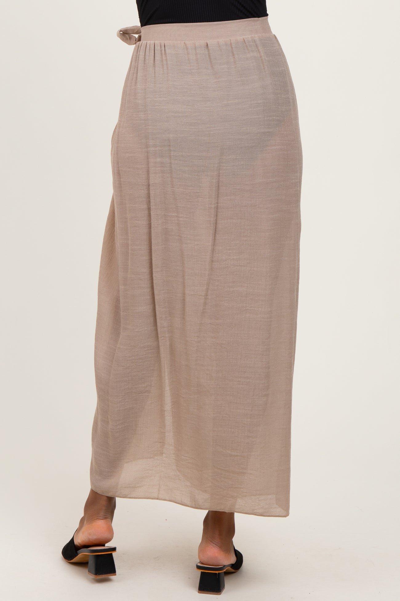 woman wearing a taupe maxi skirt with a tie detail at the waist and a flowing silhouette