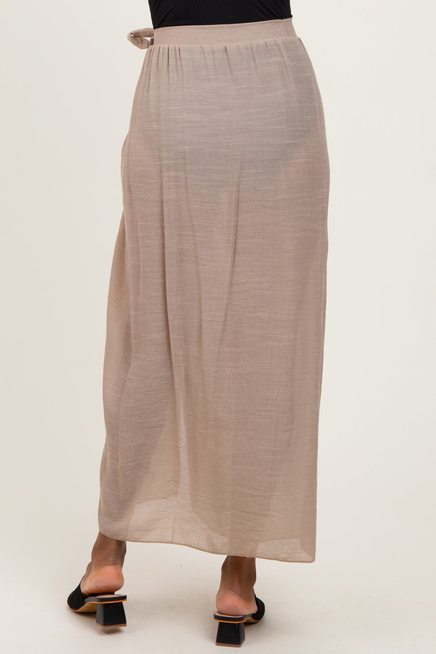 woman wearing a taupe maxi skirt with a tie detail at the waist and a flowing silhouette