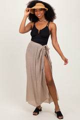 woman wearing a black ribbed swimsuit top and a tan wrap maxi skirt, accessorized with a straw hat and slip-on sandals