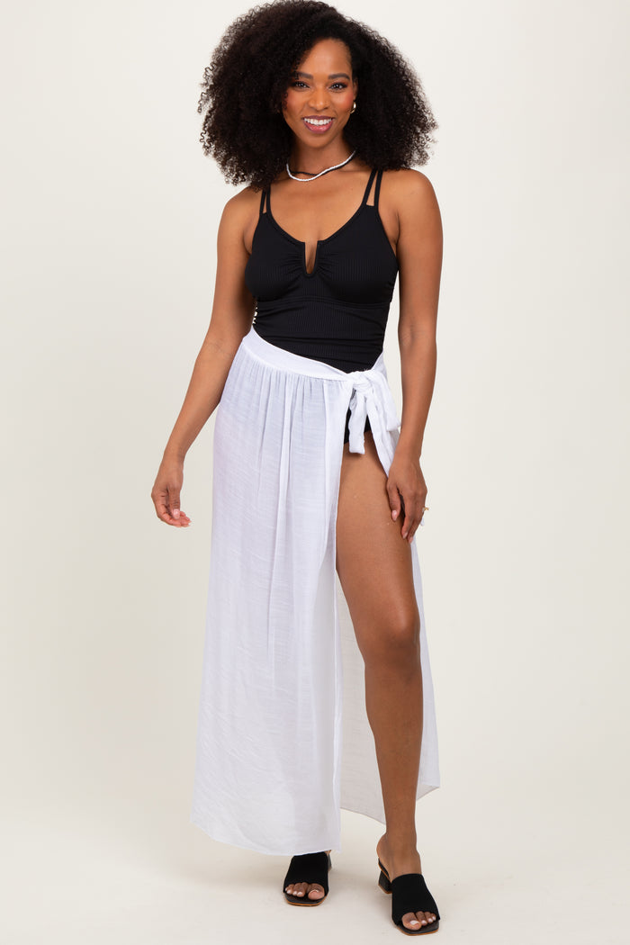 woman wearing a black ribbed swimsuit top and a white maxi wrap skirt, posing with one hand on her hip