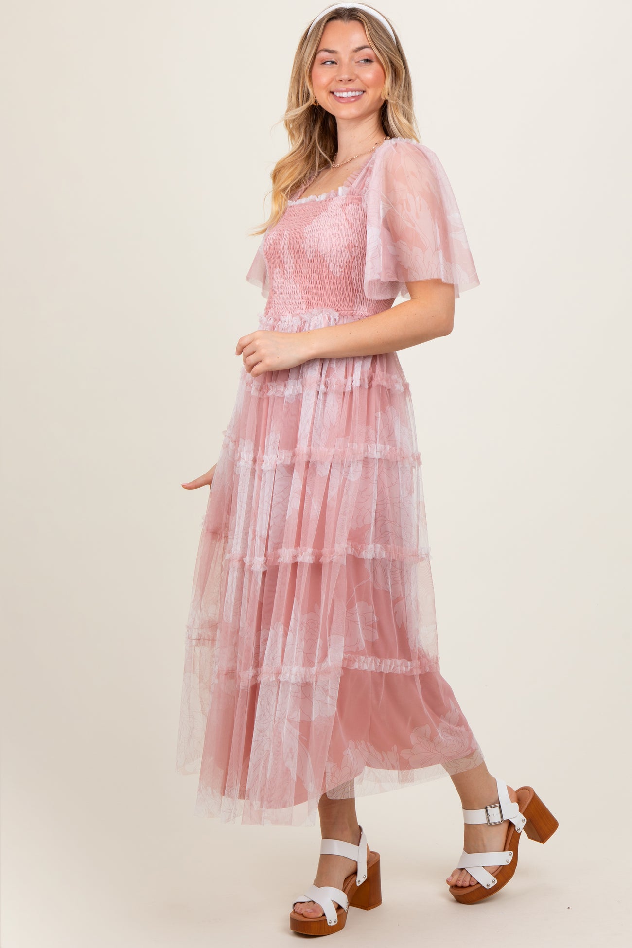 woman wearing a pink tiered maxi dress with sheer sleeves and white lace accents, standing in a relaxed pose