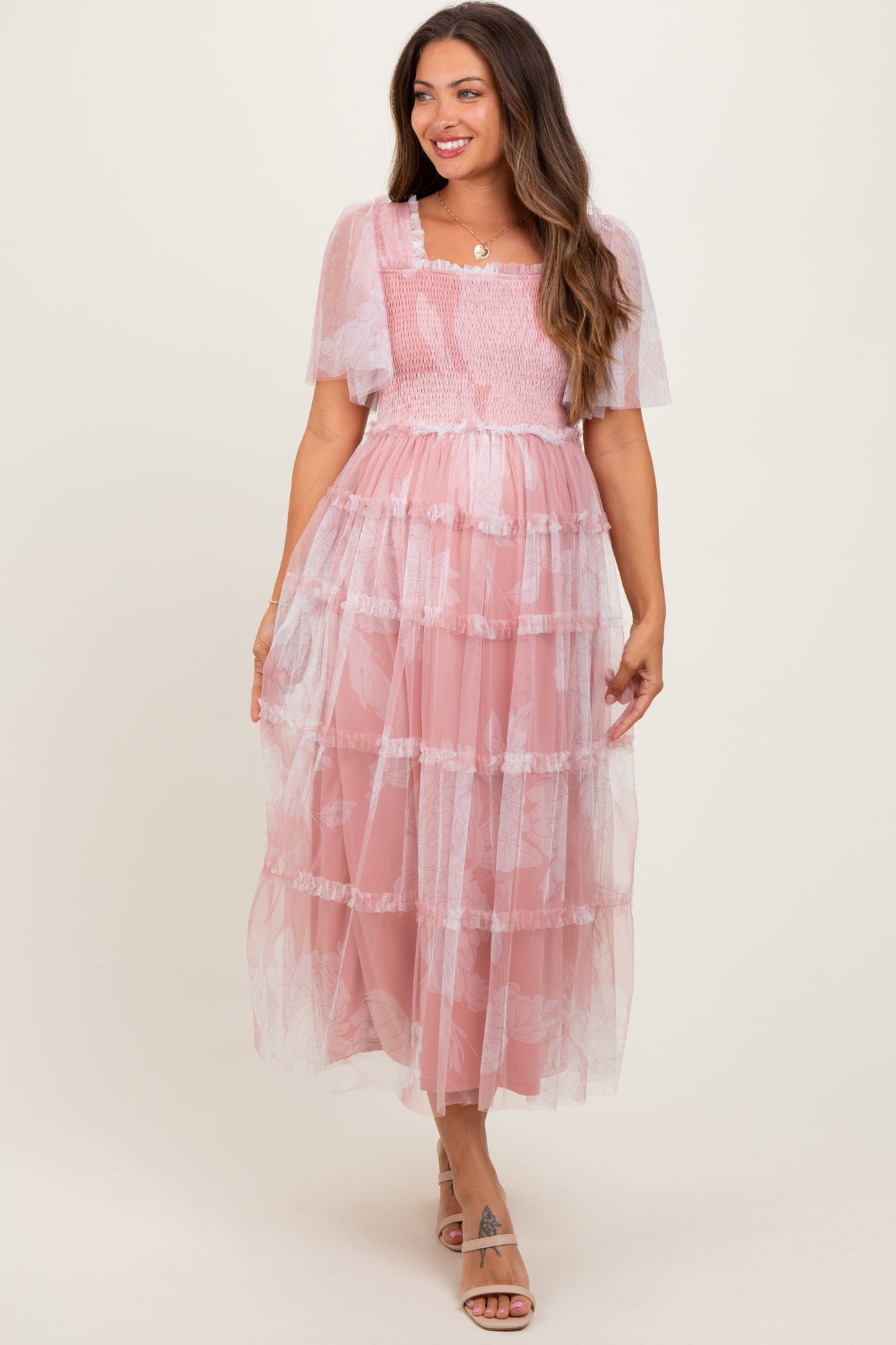 woman wearing a pink tiered maternity dress with sheer flutter sleeves and smocked bodice, featuring a visible baby bump