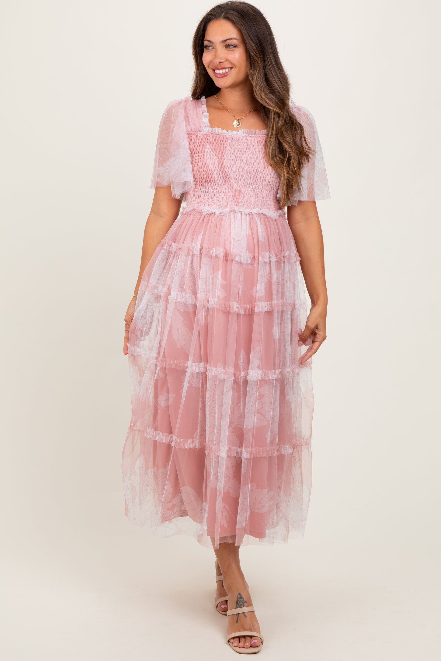 woman wearing a pink tiered maternity dress with sheer flutter sleeves and smocked bodice, featuring a visible baby bump
