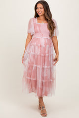 woman wearing a pink tiered maternity dress with sheer flutter sleeves and smocked bodice, featuring a visible baby bump