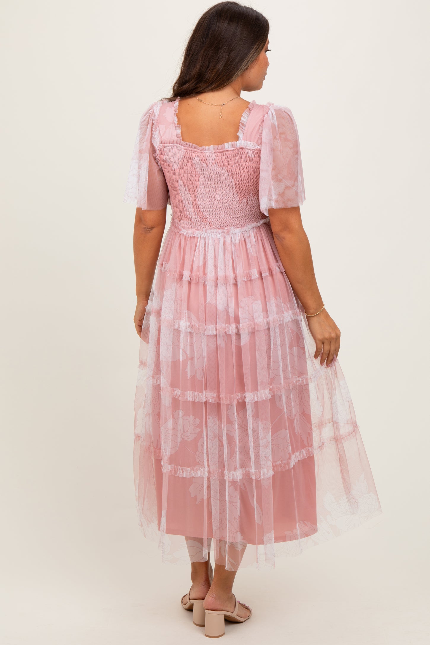 woman wearing a maternity wear pink tiered dress with floral overlay and short puff sleeves, showing a baby bump
