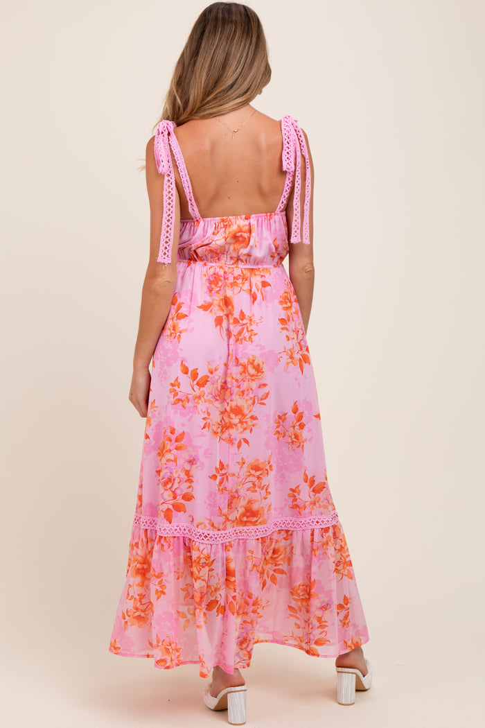 woman wearing a pink floral maternity maxi dress with adjustable tie straps and a tiered hem