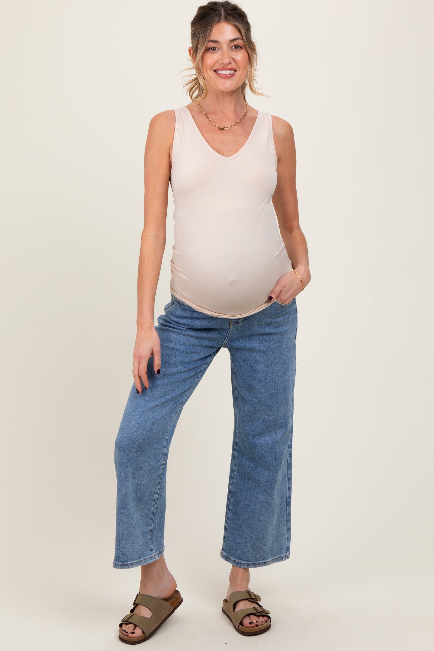 woman wearing a light pink maternity tank top and blue wide-leg jeans, showcasing her baby bump