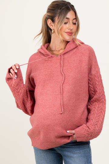 woman wearing a dusty rose maternity hoodie with cable knit sleeves and a visible baby bump, smiling and posing