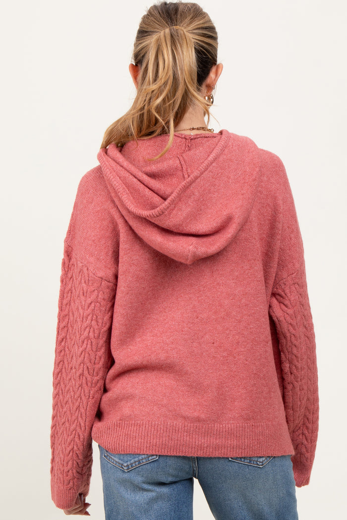 woman wearing a rose pink hooded maternity sweater with cable knit sleeves and a relaxed fit, viewed from the back