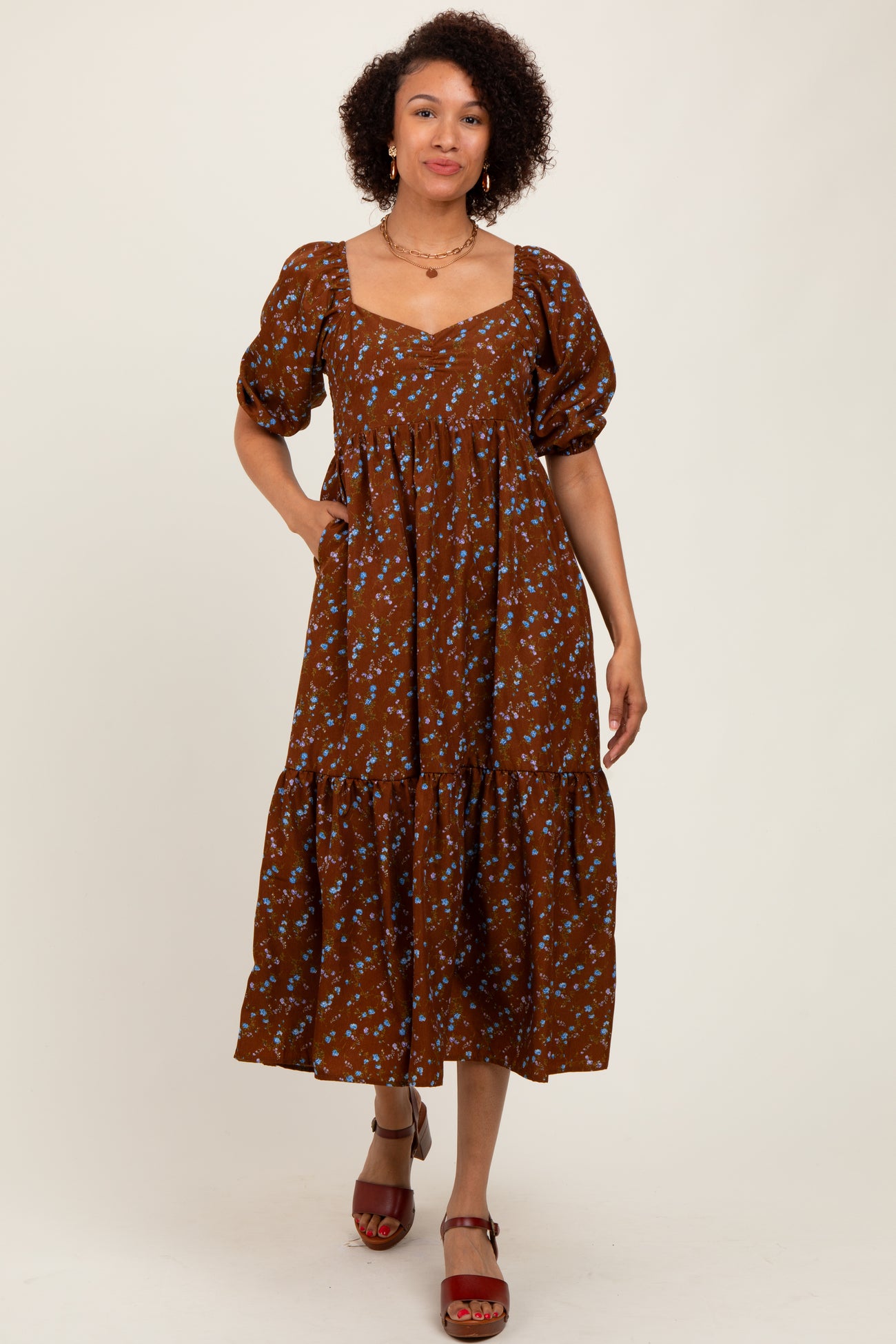 woman wearing a brown floral midi dress with puffed sleeves and a tiered skirt