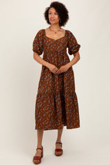 woman wearing a brown floral midi dress with puff sleeves and a tiered skirt, standing against a neutral background