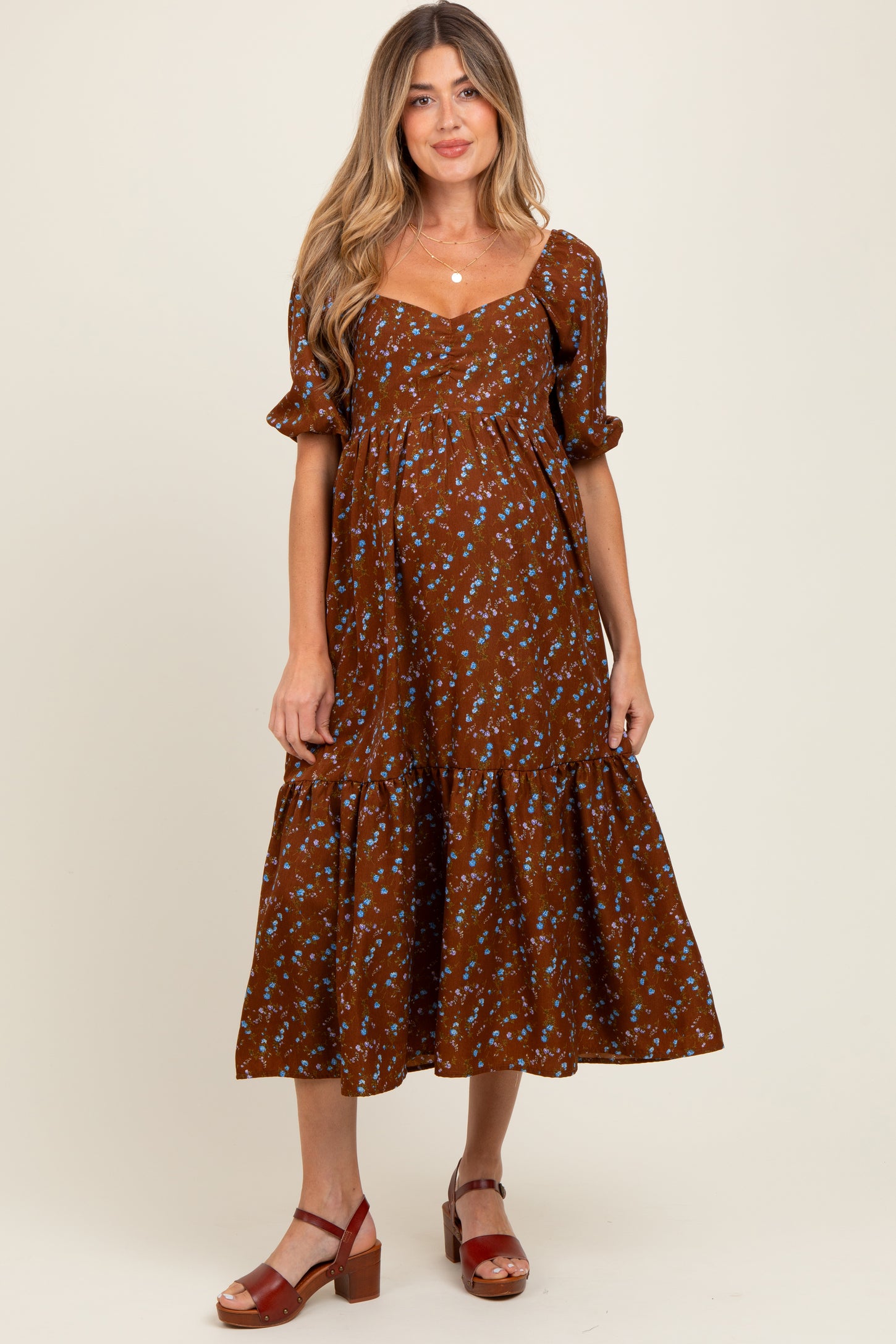 woman wearing a brown floral maternity dress with puff sleeves and a ruffled hem, showcasing her baby bump