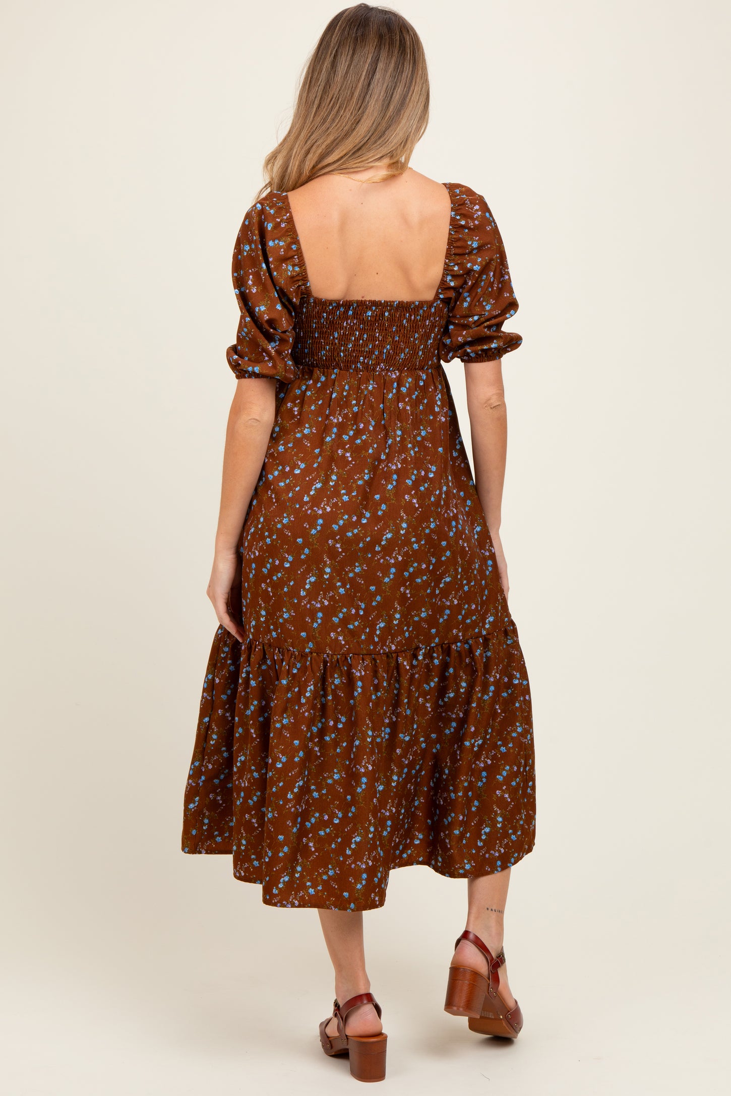 woman wearing a brown floral maternity dress with a smocked back and tiered skirt, showing a baby bump