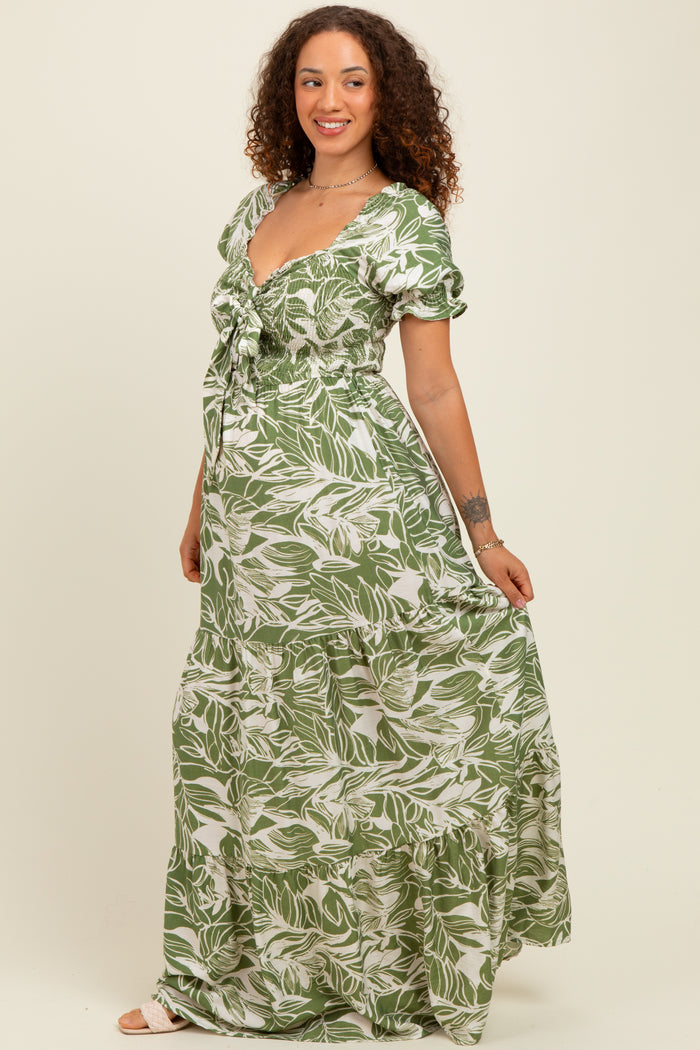 woman wearing a green floral print maternity maxi dress with short puff sleeves and a smocked bodice, showing her baby bump