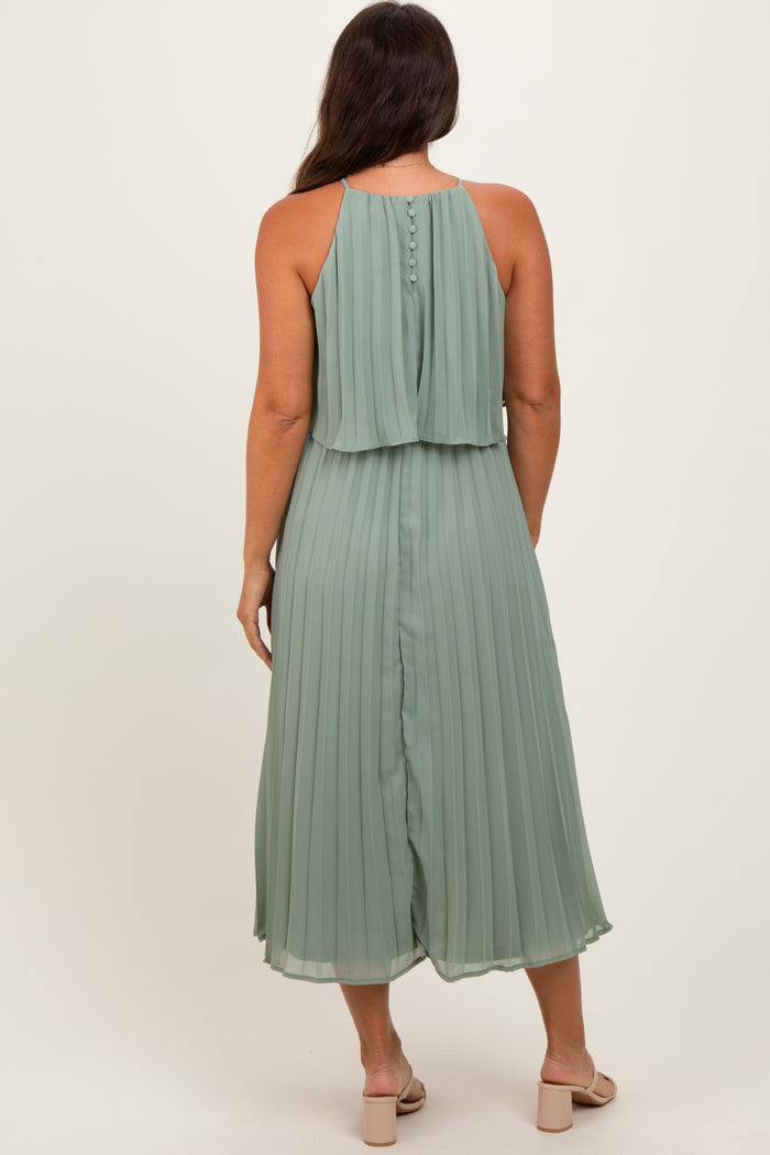 woman wearing a light green pleated maternity dress with a sleeveless design and button details at the back