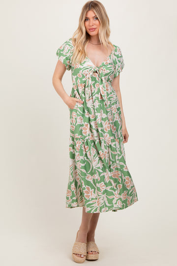 woman wearing a green floral print maxi dress with a tie front and short sleeves, standing and posing with hands in pockets