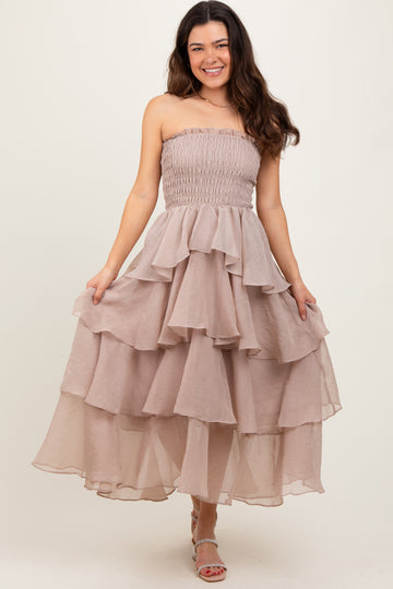 woman wearing a strapless light beige tiered maxi dress with a fitted bodice and ruffled layers
