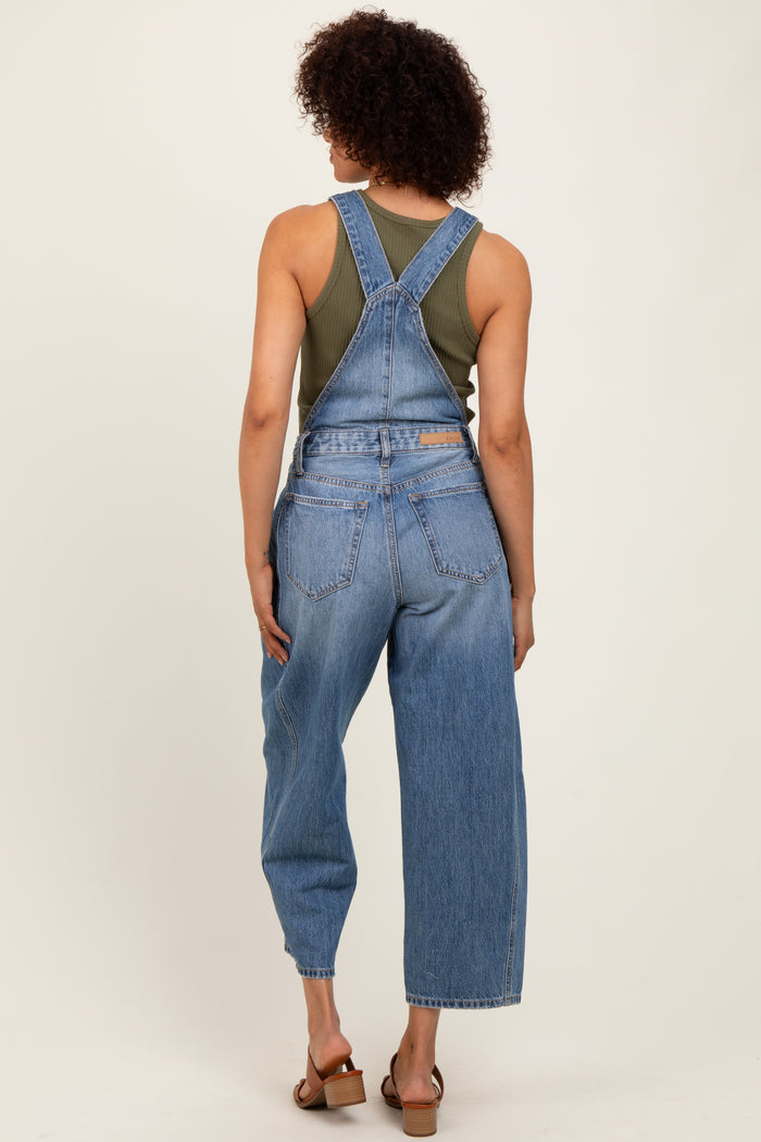 woman wearing a green tank top and blue denim overalls, showing the back view and relaxed fit of the outfit