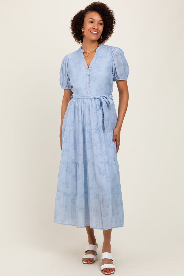 woman wearing a light blue midi dress with puff sleeves and a tie waist standing against a neutral background