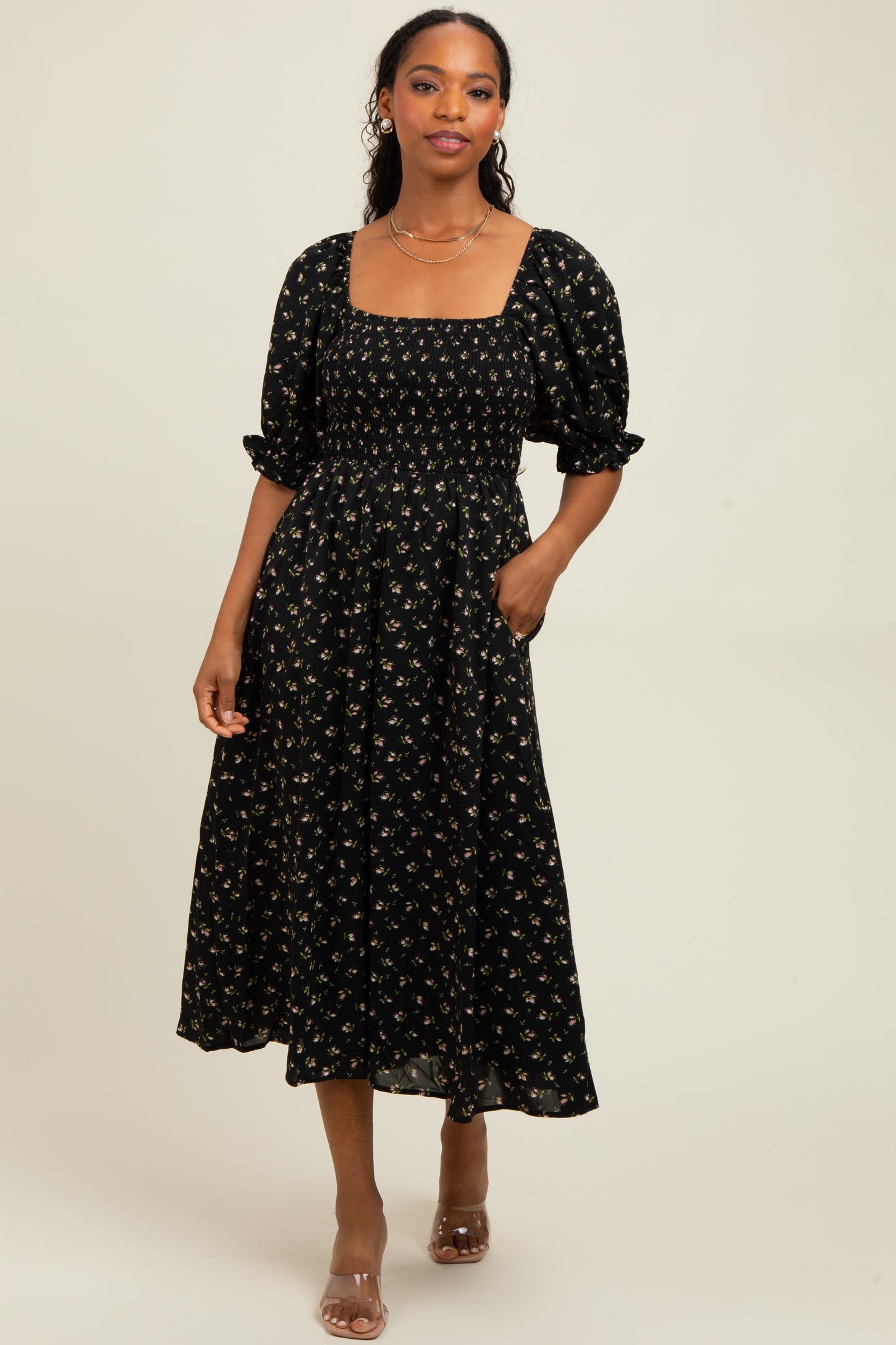 woman wearing a black floral midi dress with puff sleeves and a square neckline, posing with hands in pockets