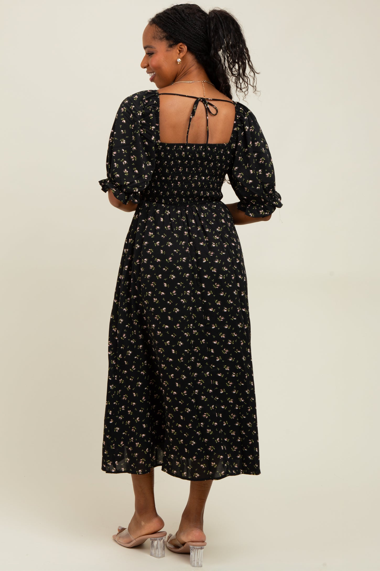 woman wearing a back view of a black floral midi dress with puff sleeves and a smocked bodice