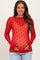 woman wearing a red sheer maternity top with black heart patterns and a visible baby bump, smiling and holding her belly