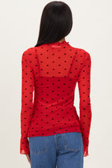 woman wearing a red sheer long sleeve top with black heart polka dots and a fitted back, paired with blue jeans