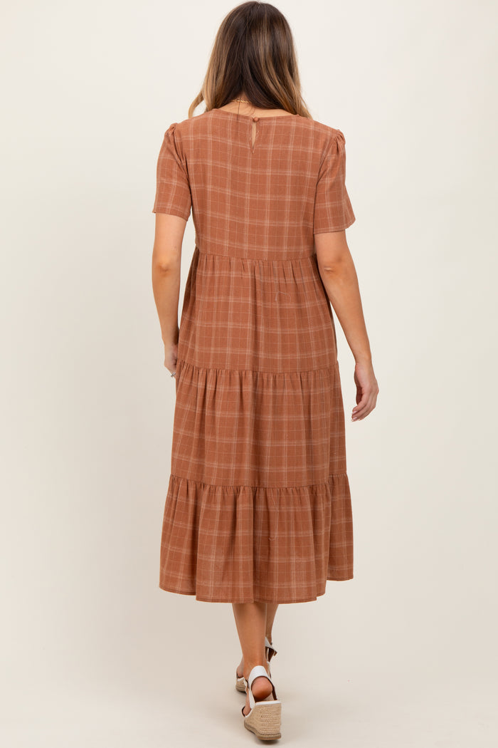 woman wearing a brown plaid tiered midi dress with short sleeves and a button detail at the back
