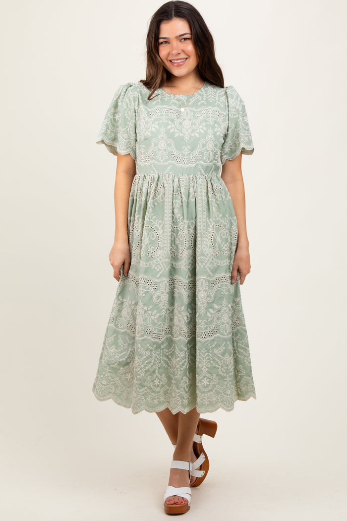 woman wearing a green lace midi dress with puff sleeves and a tiered skirt, standing and smiling