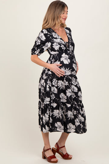 woman wearing a black floral print maternity dress with a v-neckline and tiered skirt, holding her baby bump
