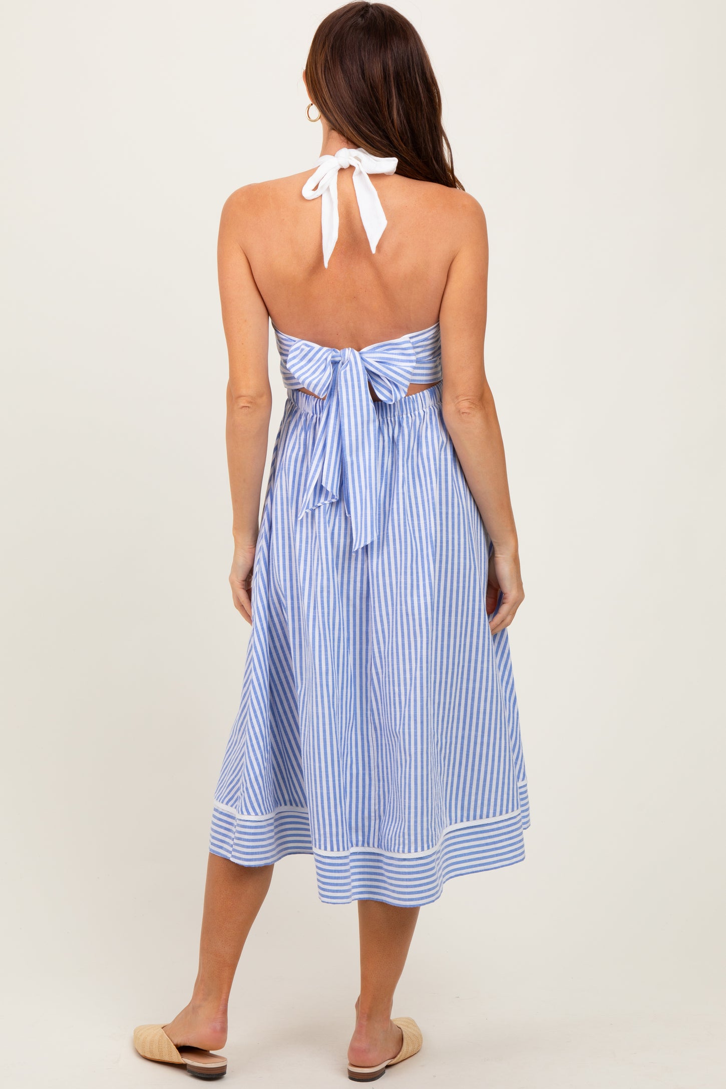 woman wearing a blue and white striped halter neck dress with a tied back detail and a midi length, shown from the back