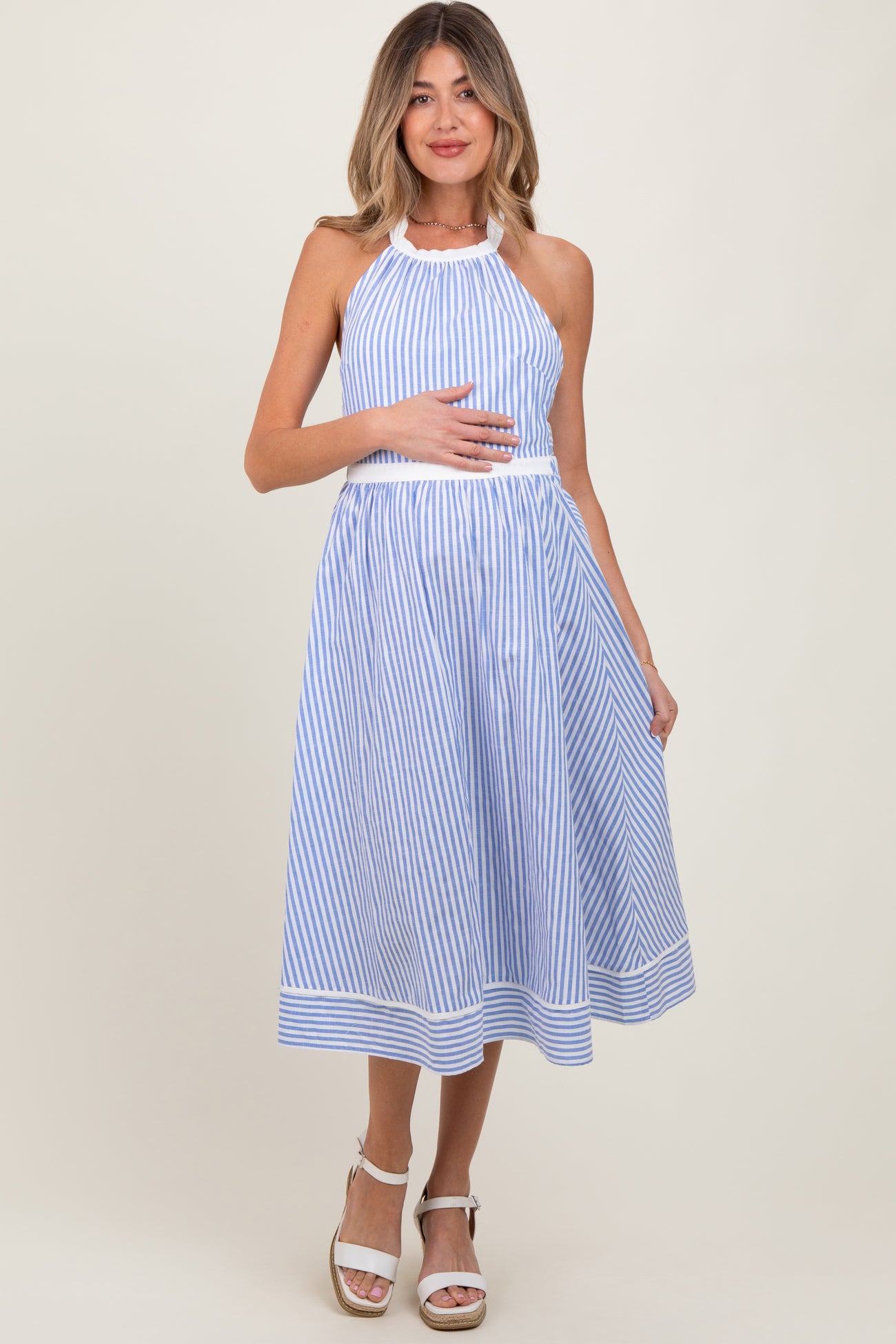 woman wearing a blue and white striped maternity dress with a halter neck, holding her baby bump