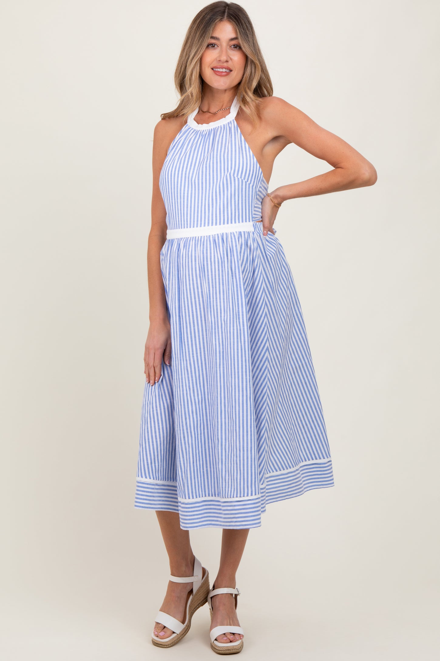 woman wearing a blue and white striped maternity dress with halter neck and flared skirt, posing with one hand on her hip