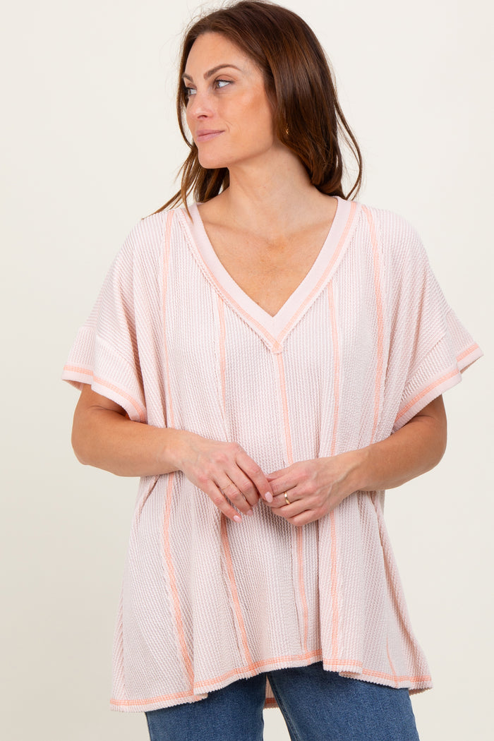 woman wearing a light pink striped short sleeve oversized top with a v-neckline and relaxed fit