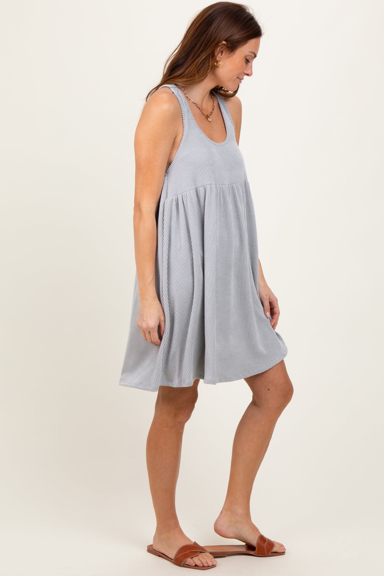 woman wearing a gray and white striped sleeveless swing dress and brown slide sandals