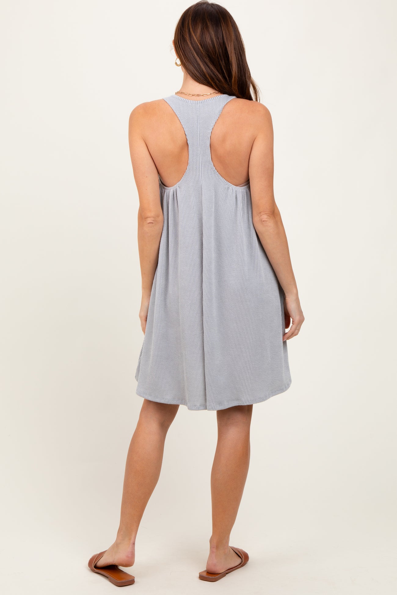 woman wearing a gray sleeveless swing dress with a racerback design, standing with her back to the camera