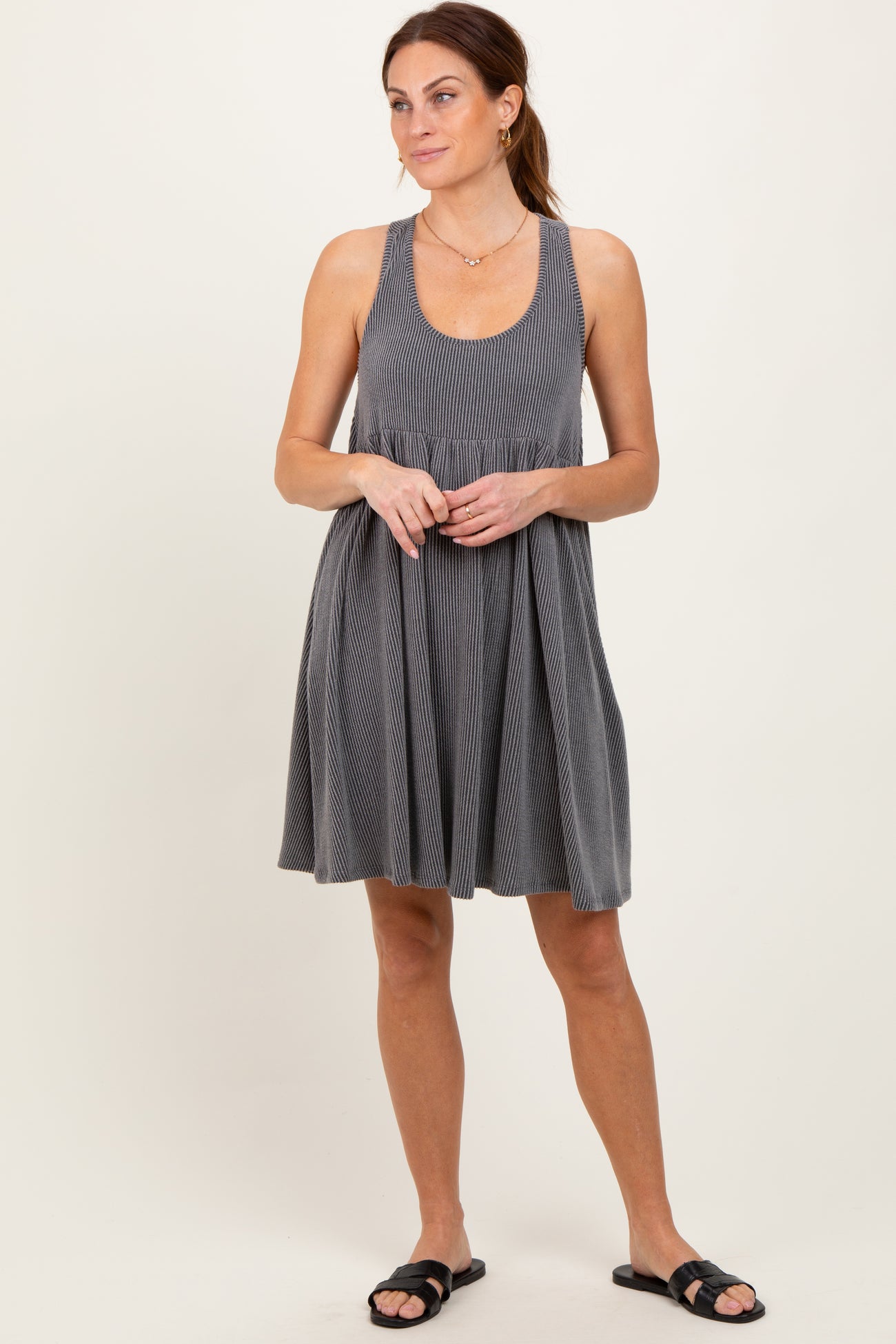 woman wearing a gray ribbed tank dress with a fitted bodice and flared skirt, styled with black slide sandals