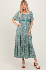 woman wearing a green floral maxi dress with short sleeves and a tiered skirt, standing on a neutral background