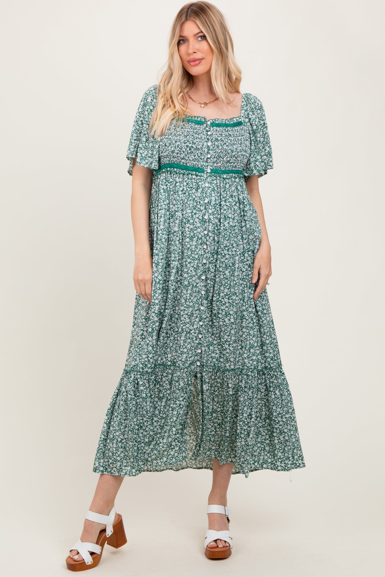 woman wearing a green floral maxi dress with short sleeves and a cinched waist, standing in a neutral background