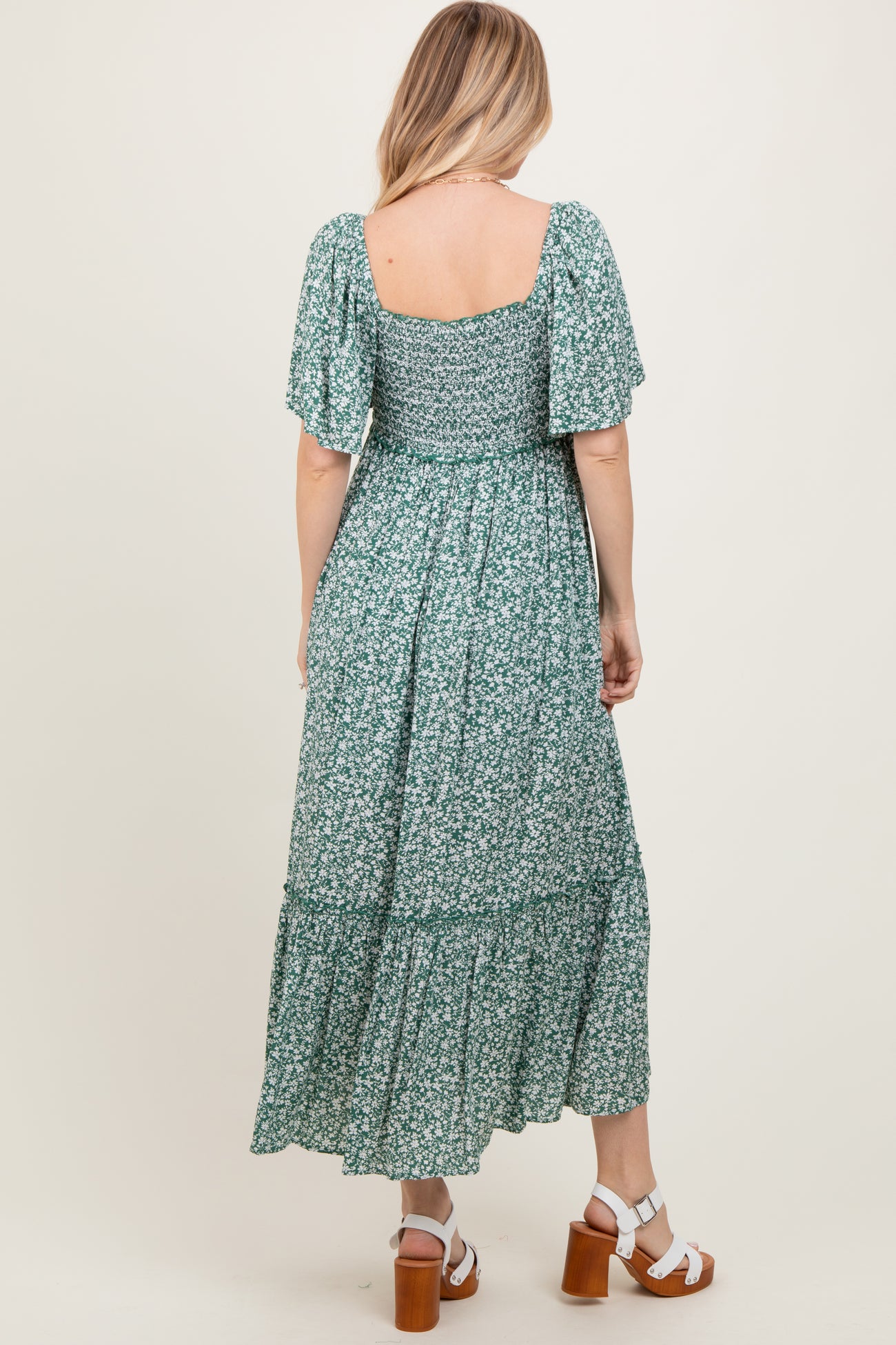 woman wearing a green floral maxi dress with short sleeves and a tiered hem, seen from the back