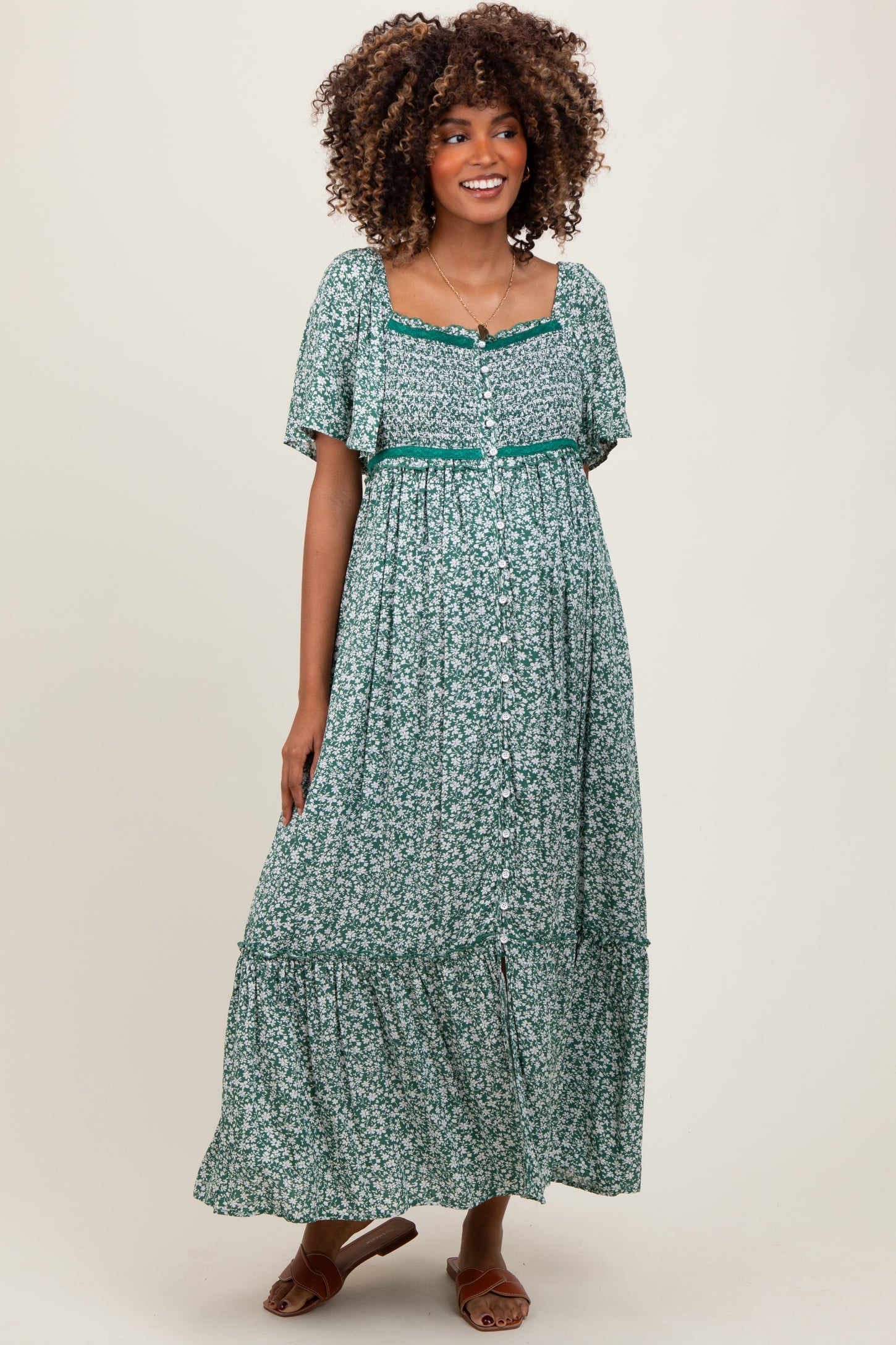 woman wearing a green floral maternity maxi dress with short puff sleeves and a tiered hem, smiling at the camera