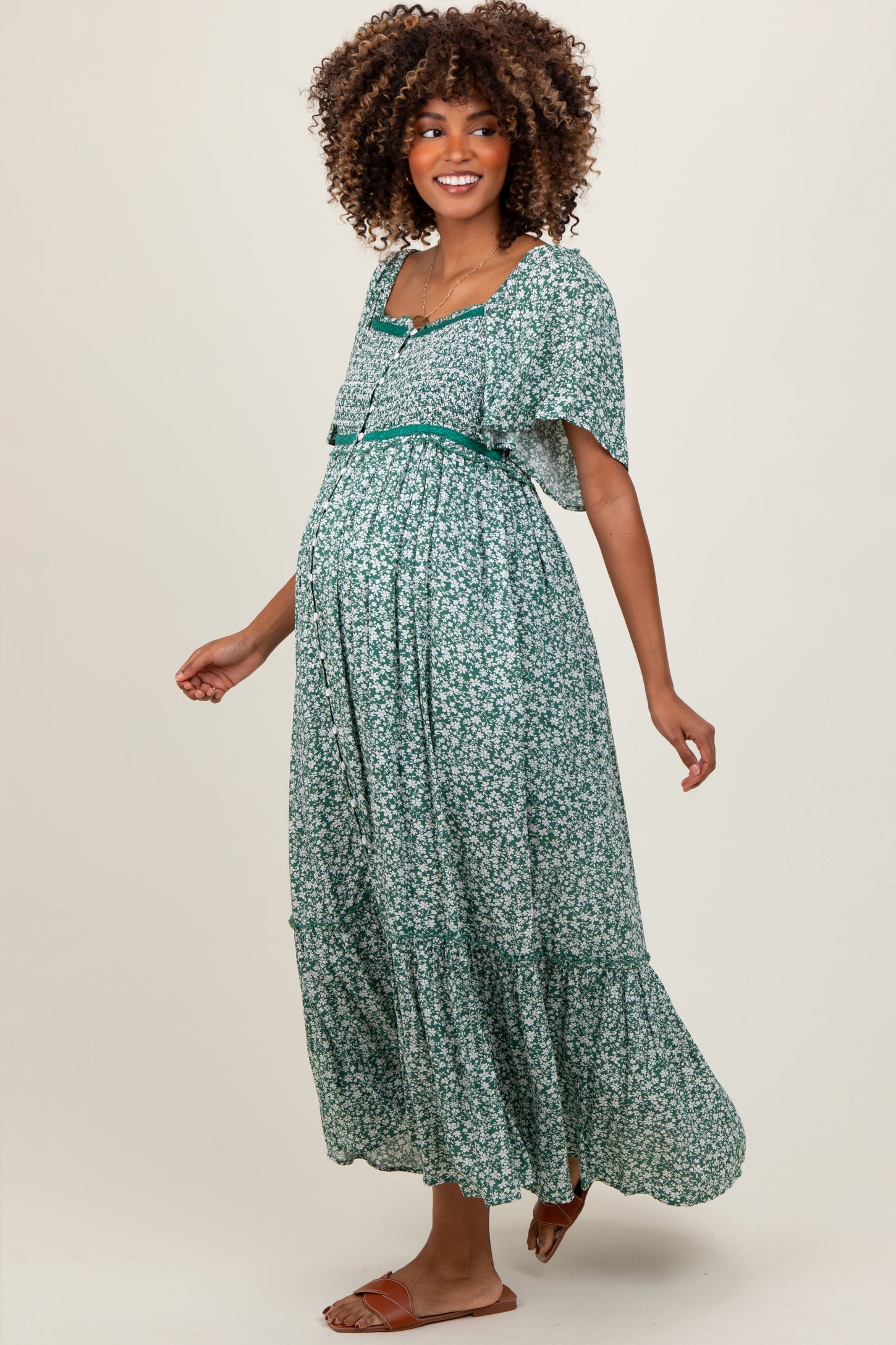 woman wearing a green floral maternity dress with short sleeves and a flowy skirt, highlighting her baby bump