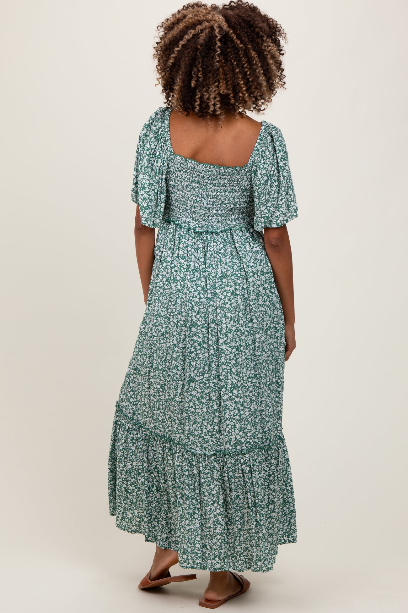 woman wearing a green floral maternity maxi dress with flutter sleeves and a tiered skirt, showing her back